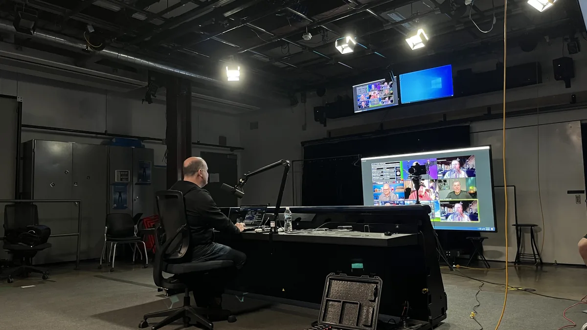 A student at the ACE-Lab control desk working across a bank of monitors showing camera feeds and a multiview