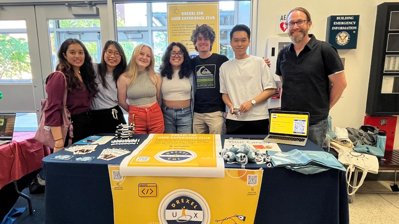Photo of the Drexel CHI UX Club board members standing and smiling next to their table at a meet and greet event